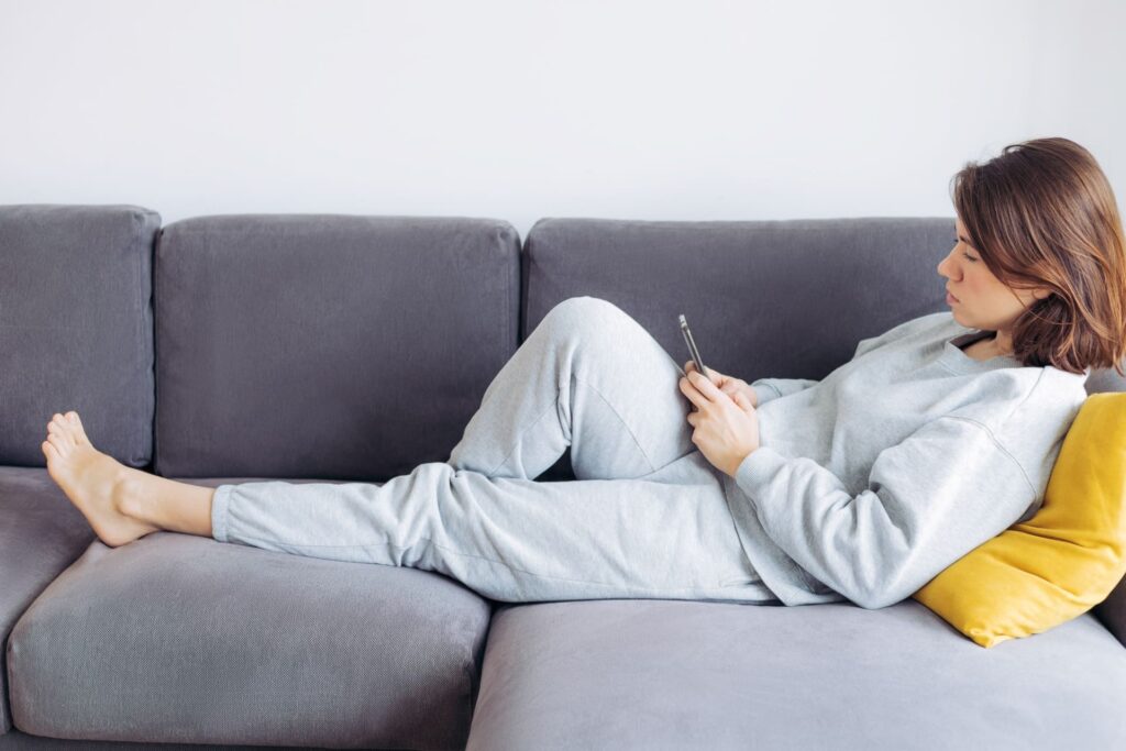 Ragazza distesa su divano con telefono.