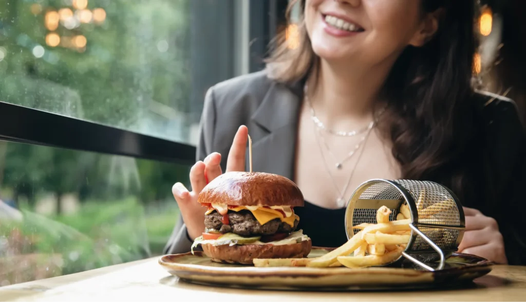 Giovane donna che ha ordinato un burger con patatine fritte