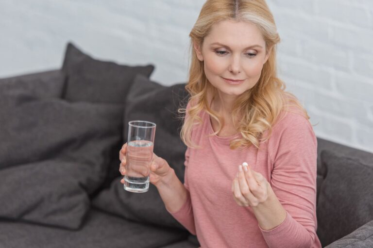 Primo piano di una donna che assume integratore con bicchiere d'acqua.