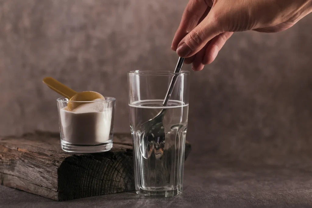 Una mano usa un cucchiaino per mescolare, in un bicchiere di vetro pieno d'acqua, del magnesio in polvere.