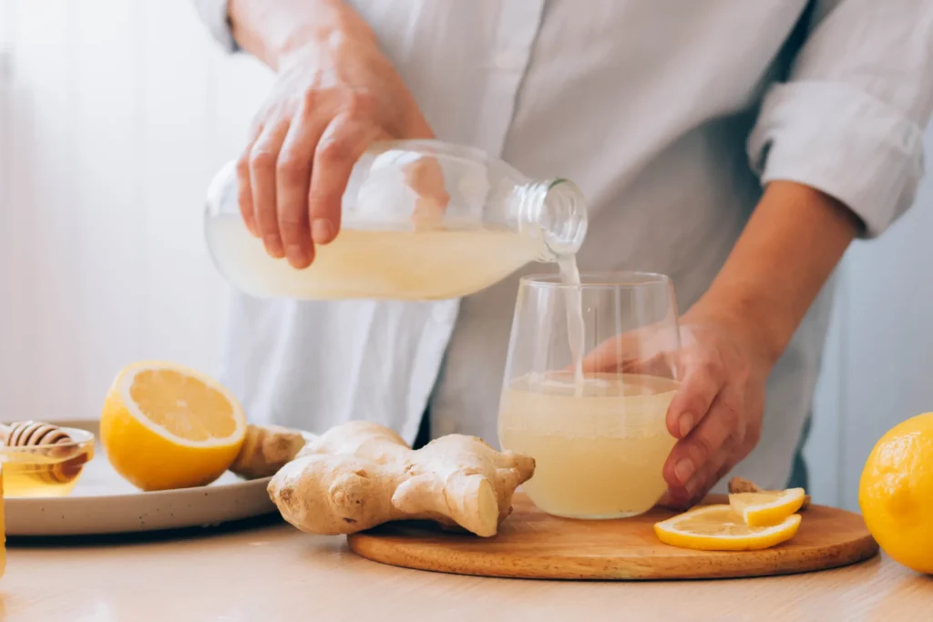 Persona che versa del succo di arancia e zenzero in un bicchiere. Sul tavolo ci sono ancora i due ingredienti freschi