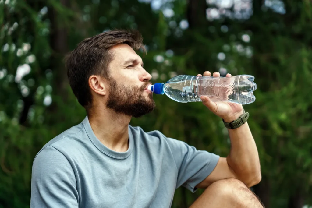 Ragazzo sportivo beve una bottiglia d'acqua all'aperto