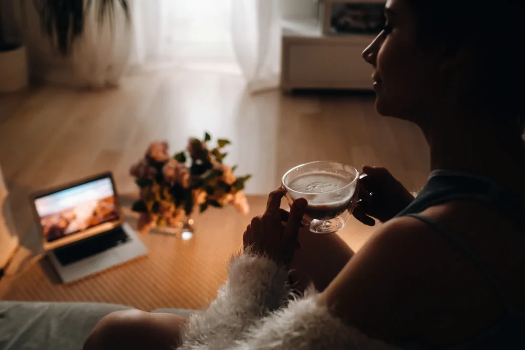 Giovane donna si rilassa a casa sua guardando un film al computer e bevendo una tazza di tè