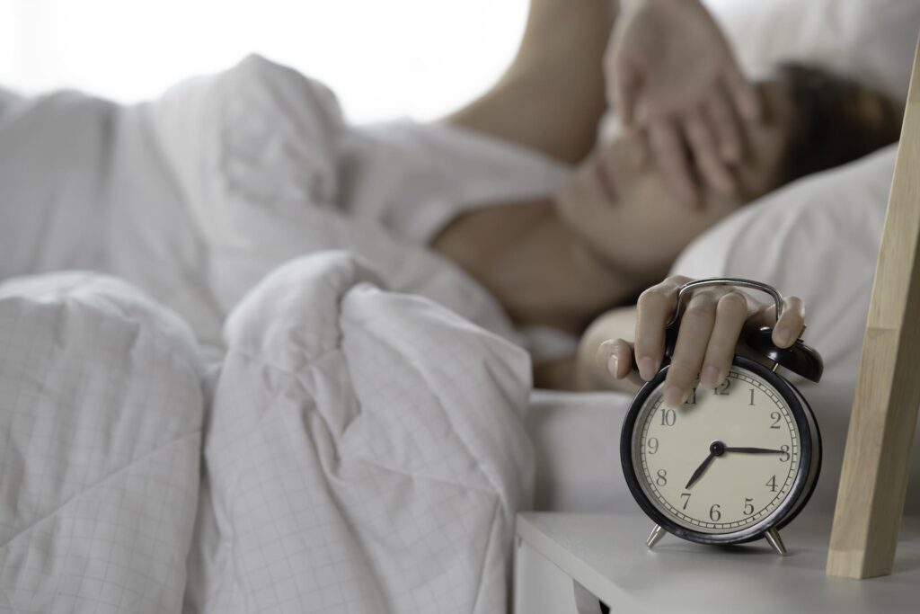 Donna che spegne la sveglia a letto con difficoltà a causa di stanchezza al mattino.