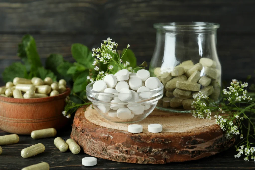 Compresse tonde bianche e compresse ovali verdi racchiuse in due ciotole di vetro, poggiate su un ripiano in legno e circondate da fiorellini bianchi ed erbette