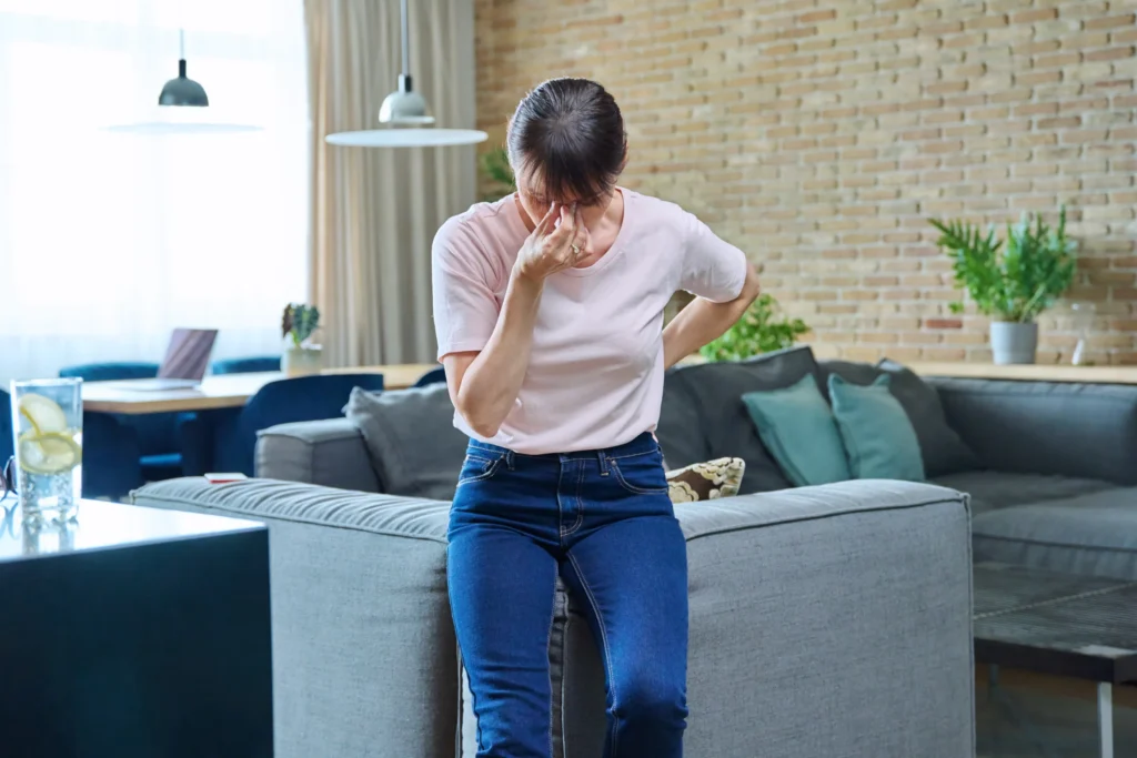 Donna di mezza età, appoggiata al divano, mentre si tocca gli occhi