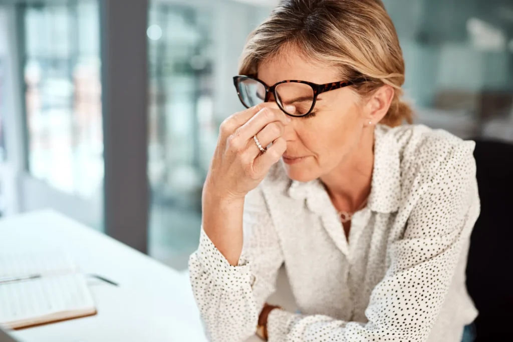 Donna sui 50 anni in ufficio che si tocca il naso alzando gli occhiali da vista