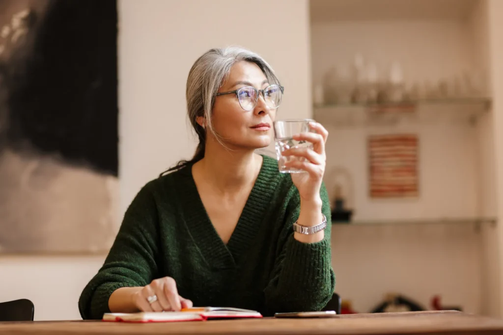 Donna sui 50 anni seduta in casa con un bicchiere di acqua in mano