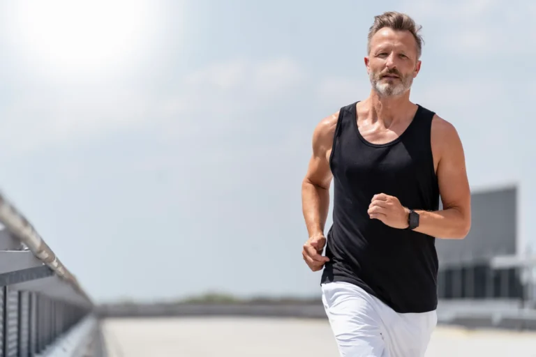 Uomo brizzolato che corre all'aria aperta indossando una canotta nera e pantaloncini bianchi