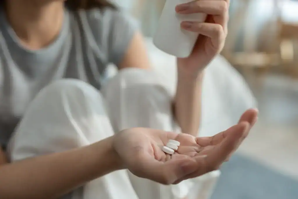 Primo piano delle mani di una donna che prende un integratore dopo essersi svegliata a letto.