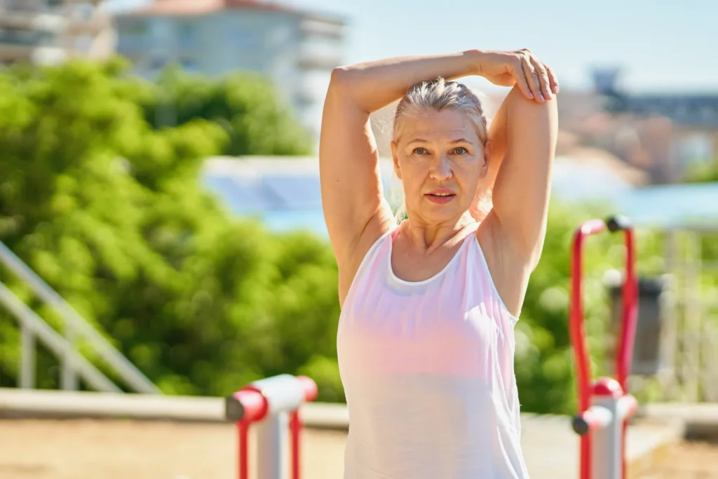 Una donna fa streching sulle spalle all'esterno, in una giornata di sole