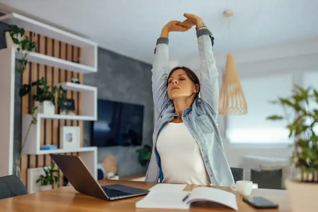 Donna che fa stretching alla scrivania in un luminoso ufficio domestico
