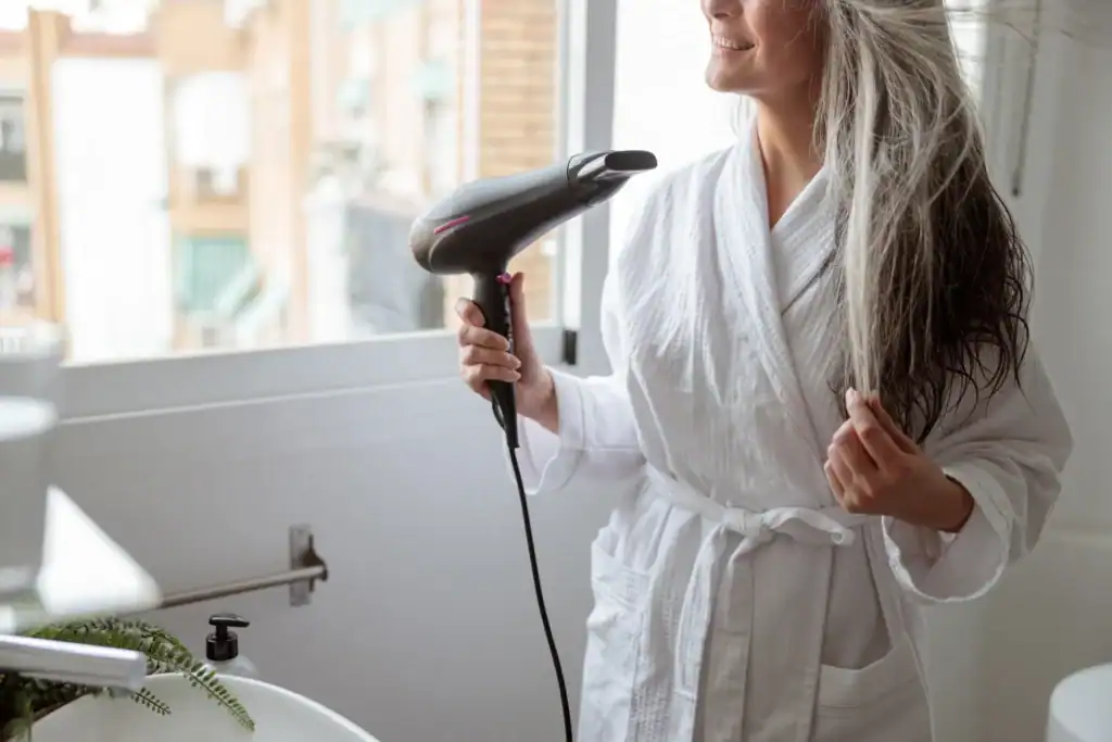 Donna in accappatoio si asciuga i capelli in un bagno soleggiato